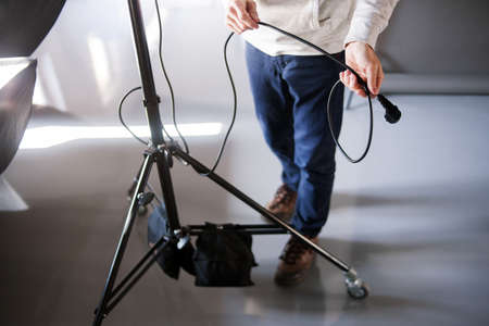 Assistant work with tripod in photostudio. Unrecognizable man setting the photo equipment. Professional photographer is adjusting studio for photographing.の写真素材
