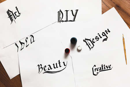 Sheets of paper with inspirational words drawn with ink. Top view. Painter workshop, business inspiration, calligraphy, creativity conceptの写真素材