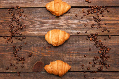 Roasted coffee beans frame and croissant on wooden background. Closeup of seeds on dark brown cafe table. Top view.の写真素材