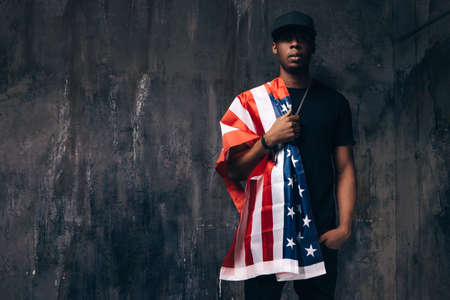 Black man with american flag on shoulder on dark background. Patriot, national event celebration, independence day, pride, immigration, us citizenship conceptの写真素材
