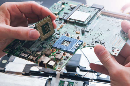 Technician plug in CPU microprocessor to motherboard socket. Workshop background