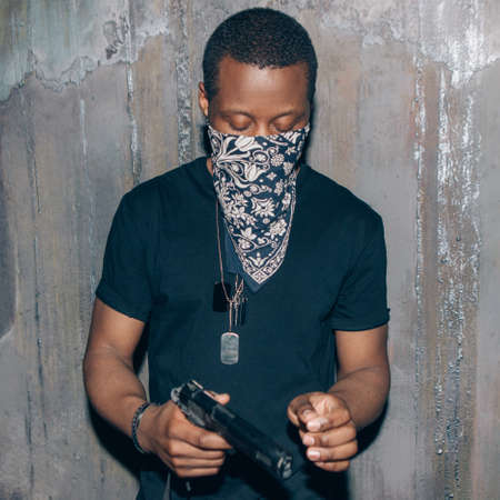 Black mercenary mercenary with gun. Gangster man with weapon in hand on dark gray background....