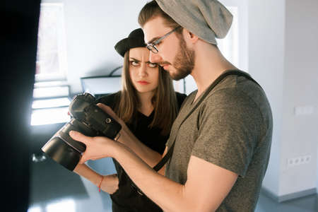 Conflict with photographer on photoshoot. Model didnt like photos on camera. Man with camera show pictures to angry woman in during the studio session.の写真素材