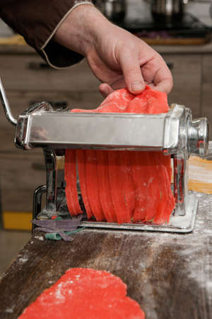 Chef with pasta machine cooks red noodles dough. Colorful food concept closeupの写真素材