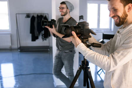 Two laughing professional photographers taking shots in studio. Happy moments at work, joke, have a...