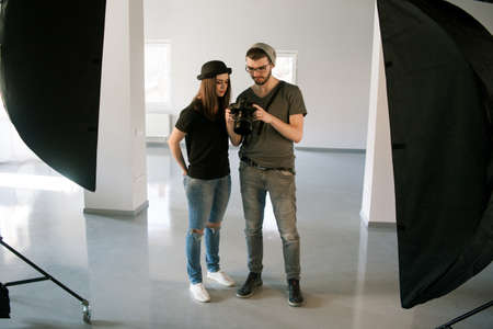 Photographer speaks with model on photoshoot. Man with camera show pictures to casual woman during...