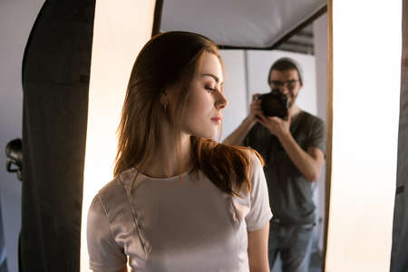 Photo session backstage. Photographer shoot woman. Back view from models shoulder on studio interior...