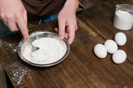 Chief mixes flour with eggs in bowl on wooden table, preparation food concept top view