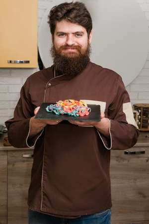 Happy bearded chef on kitchen with color pasta. Macaroni cooking processの写真素材
