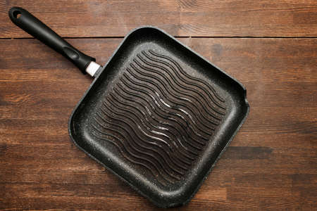 Empty square grill pan on wooden table. Black kitchenware top viewの写真素材