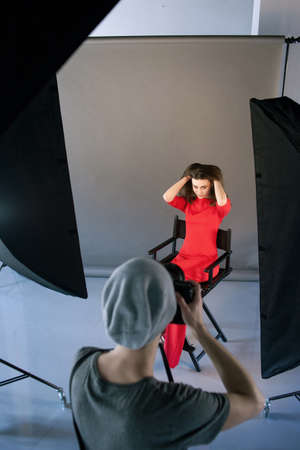 Photographer shoot model in red at studio session. Unrecognizable man taking shot of female model in studio. Photo school, lookbook, fashion backstage conceptの写真素材