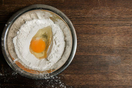 Egg and flour mix in plate on wooden table. Baking process concept, wooden background with copy spaceの写真素材