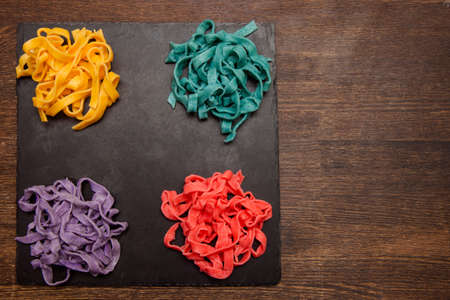 Colorful tagliatelle on black plate on table. Creative food concept top view, free space on wooden backgroundの写真素材