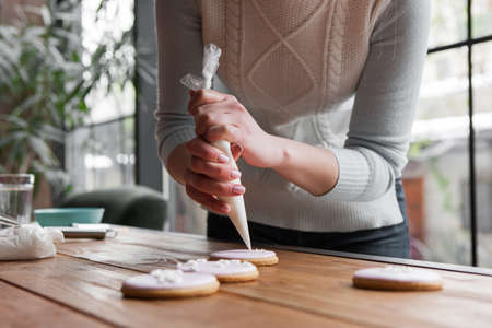 Female chef decorating pink gingerbread with pastry bag. Cooking background, sweet food. Tasty...