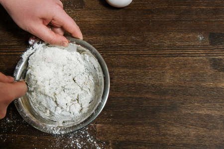 Chief mixes dough in bowl on table. Food concept, wooden background with free spaceの写真素材
