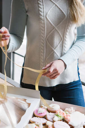 Girl decorating gingerbread box with ribbon. Female courier, baking closeup, sweet dessert, tasty food conceptの写真素材
