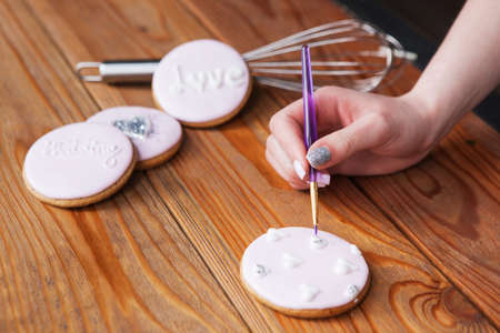 Gingerbread decorated with icing by female baker. Sweet dessert on woooden background, colorful cookie, wedding present closeup. Tasty food, bakery conceptの写真素材
