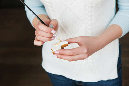 Female baker decorating gingerbread with brush. Food process, sweet dessert. Unknown person, tasty...