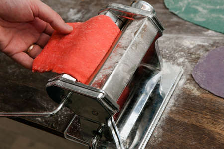 Closeup pasta machine process with red dough noodles on wooden table. Top view colorful food conceptの写真素材
