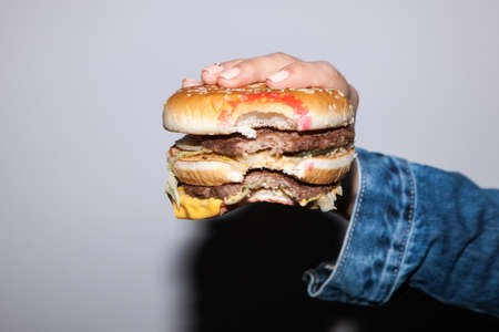 Burger holding in hand on gray background. Junk food concept in lifestyle of peopleの写真素材