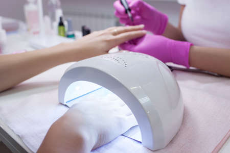 UV lamp gel polish manicure process. Salon procedure. The master coats the clients nails with a varnish.の写真素材