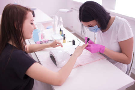 Professional manicure procedure. Gel polish on the nails. Female master in the salon work with hands of the client. Beauty industry, relax concept.の写真素材