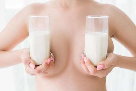 Two glasses of milk partially close woman breasts. Lactation and healthcare concept during maternity periodの写真素材