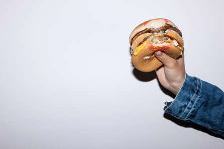 Fast food burger holding in hand on white background. Junk food concept in lifestyle of peopleの写真素材