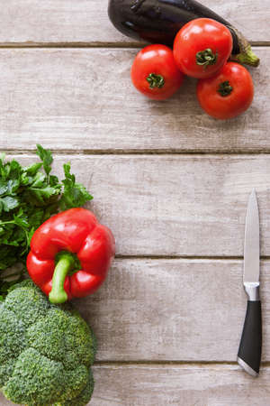 Fresh ripe vegetables on white wooden background and copy space. Red tomatoes and pepper, broccoli, eggplant, parsley and steel knifeの写真素材