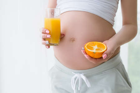 Fresh orange juice in hands of pregnant woman. Healthy food and drink, body and healthcare concept of special mother-to-be periodの写真素材