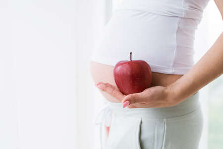 Ripe apple in hands of pregnant woman. Healthy food and drink, body and healthcare concept of special mother-to-be periodの写真素材