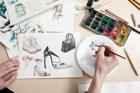 Fashion designer mixes colours of paint in process of drawing fashion sketches of footwear and clothingの写真素材
