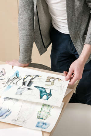 Designer work on fashion sketches. Unrecognizable man with pictures of clothes and footwear in...