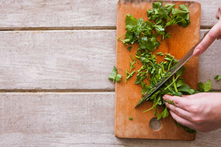 Woman cuts batch of parsley on wooden desk with steel knife. Herbs as healthy and organic food, top view picture, free space nearbyの写真素材