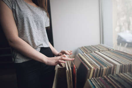 Choosing retro vinyl records. Music background. Unrecognizable woman in musical shop, old school hipster styleの写真素材