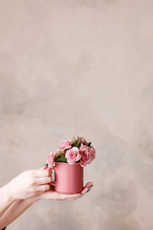 Beautiful pink roses in crimson cup holding in hands on beige background. Concept of love, romantic gift and flower decoration, holidays and congratulations, free spaceの写真素材