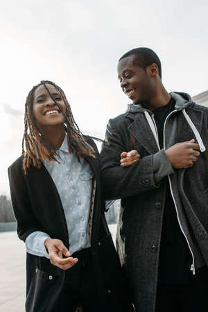 Joyful romantic date. Happy black couple outdoor. African American pedestrians laughing, sky background, street fashion style, happiness conceptの写真素材