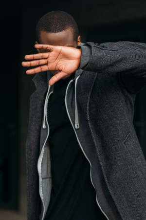 African American male introvert. Bright light. Stylish black man protecting himself, unrecognizable guy covering face on dark background, fear conceptの写真素材