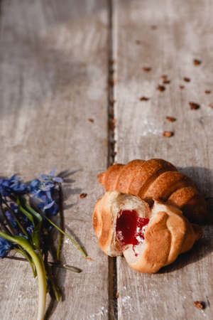 Delicious breakfast on wooden background. Sweet croissant with fruit jam and granola with spring blue snowdrops nearby. Morning fresh and tasty meal. Food photography close upの写真素材