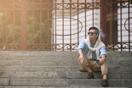 Young smoking man on coffee break on urban background. Bad habits. Unhealthy lifestyle, modern student life, hipster conceptの写真素材