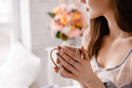 Beautiful young lady with cup of morning coffee in hands. Sunrise enjoyment and calmness, positive...