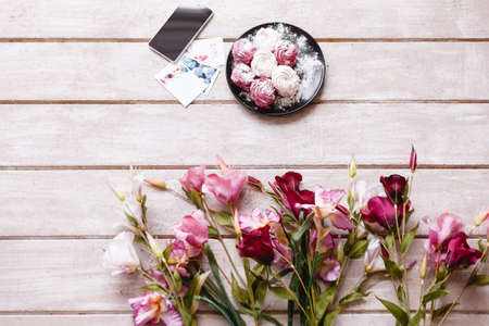 Sweet and blossomed background on wooden backdrop. Colorful zephyrs on plate and white, pink and deep purple eustoma, smartphone and post cards with free space nearbyの写真素材
