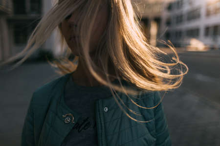 Girl portrait with windy hair in motion closeup. Easiness after break up, young independent woman in cityの写真素材
