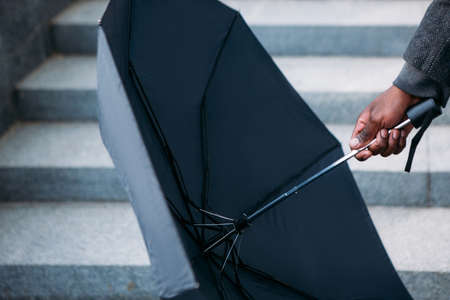 Rainy weather. Modern urban lifestyle. Unrecognizable black male on street, umbrella in selective focusの写真素材
