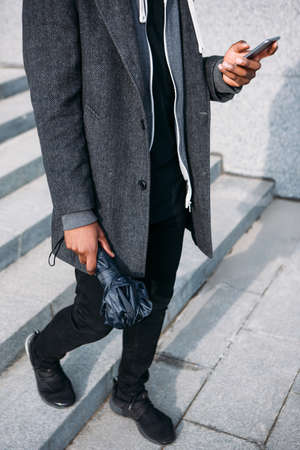 Social media communication. Fashion street style. Unrecognizable black male outdoors, rainy grey weather, modern technologyの写真素材
