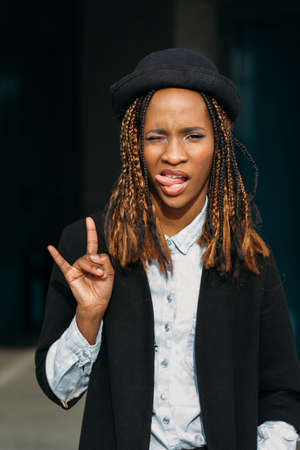 Rock gesture. Modern young black lady. Playful African American woman on dark background in selective focus, stylish female, joy conceptの写真素材