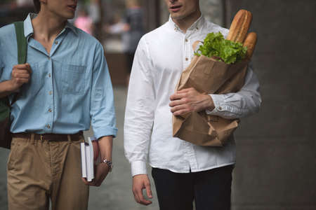 Two stylish pedestrians outdoors. Men shopping. Unrecognizable male students, healthy food for youth, communication conceptの写真素材