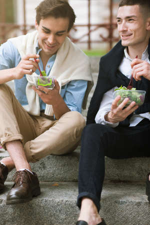 Two happy men with healthy food outdoors. Male street style. Lunch break, stylish joyful young people, diet conceptの写真素材