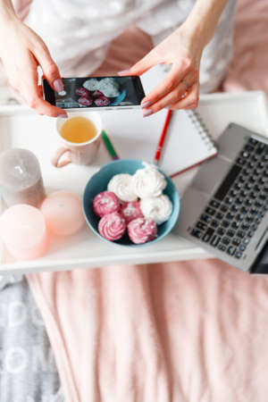Unrecognizable woman makes photo of sweets by smartphone. Food photography of zephyrs during process of breakfast and chatting for social media, top viewの写真素材
