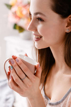 Beautiful smiling girl with cup of morning coffee in hands. Advertizing of positive energy charge for whole day, sunrise enjoyment and relaxation, sensuality and comfort concept, close upの写真素材